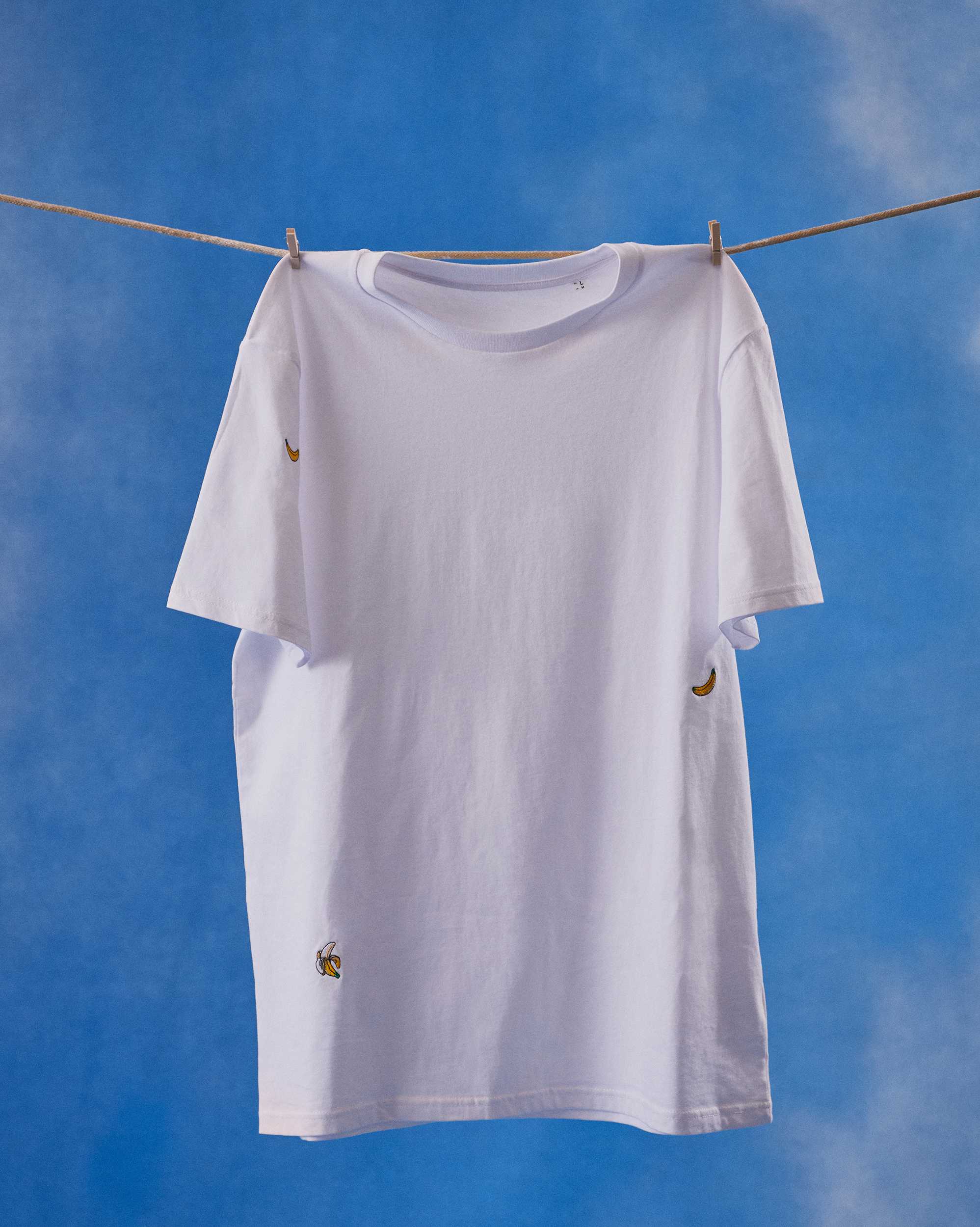 A white t-shirt with banana embroideris haging to dry on a line 