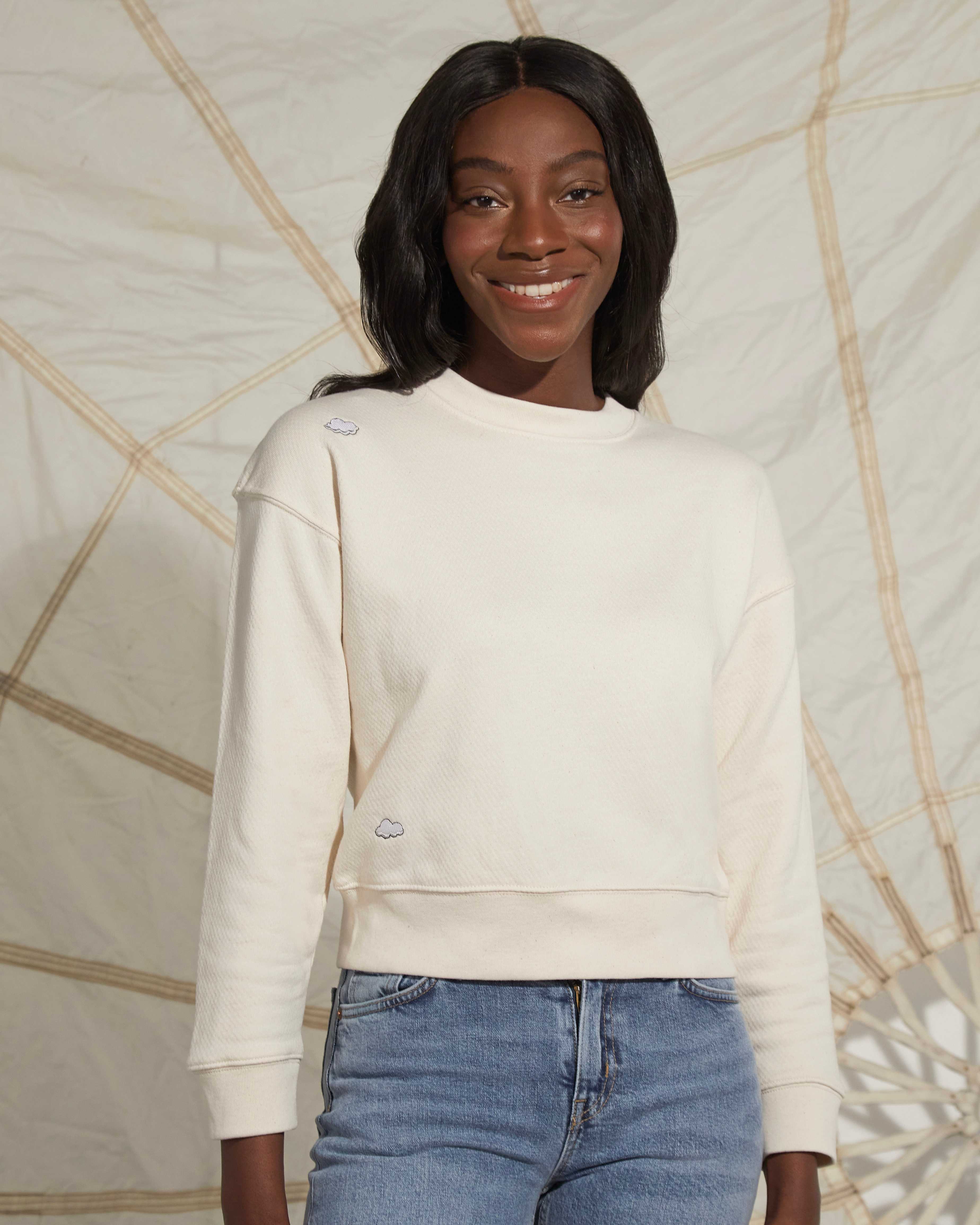 Women wearing a cream ingmarson sweatshirt with clouds embroidered and blue levis jeans posing infront of a parachute 