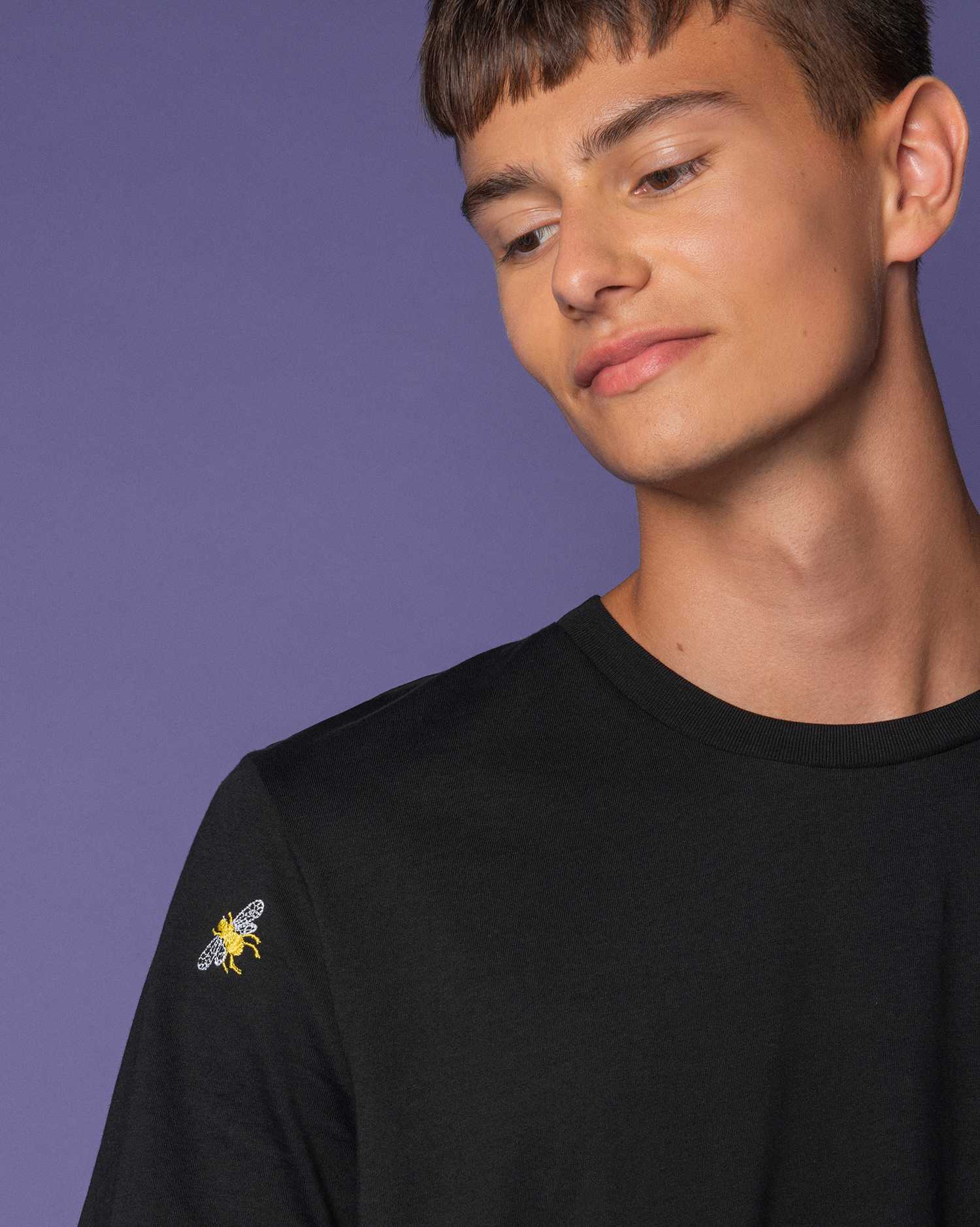 A man wearing a black tshirt with bees embroidered 