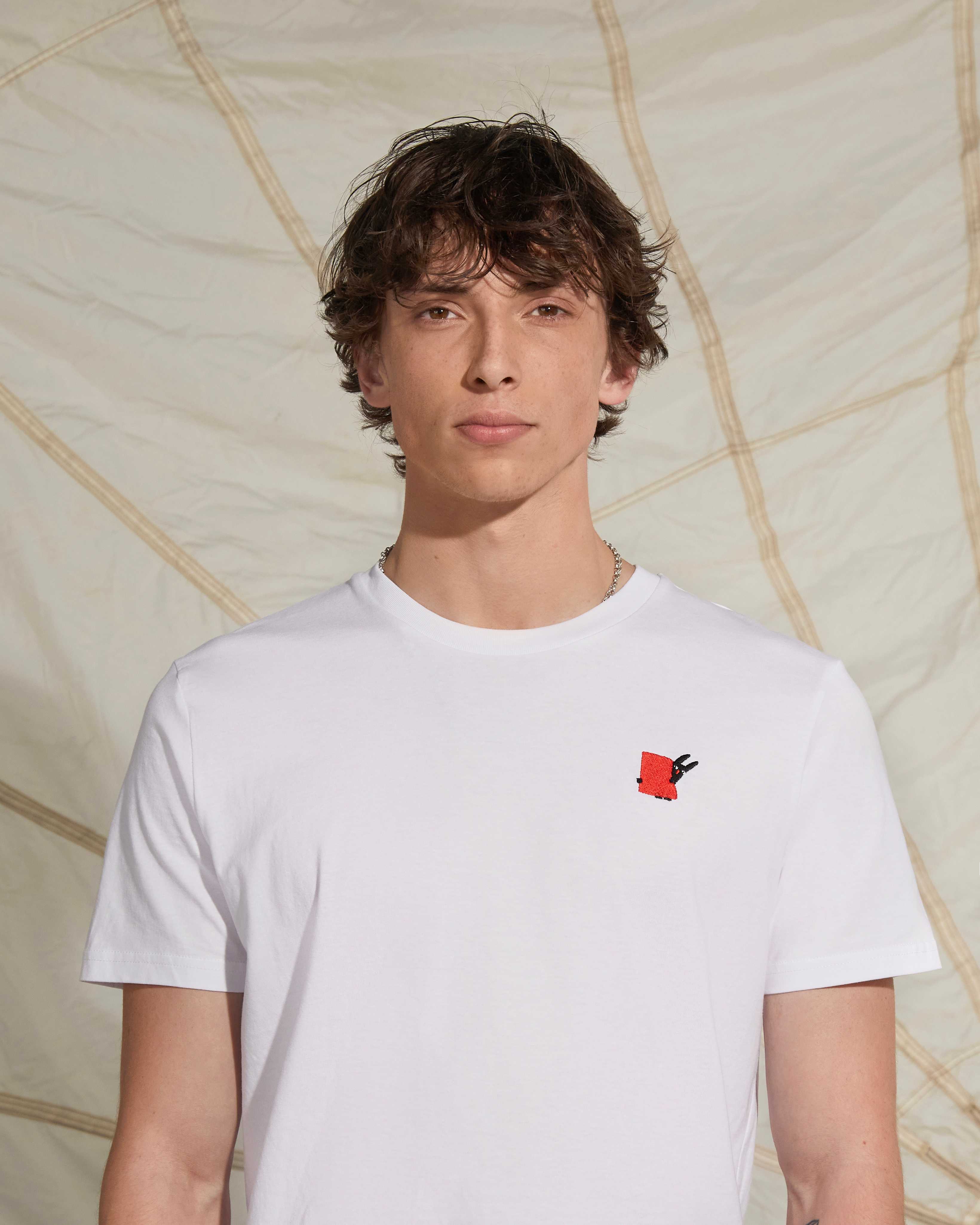 A man wear a white t-shirt with a red chest embroidery by Pierre Buttin
