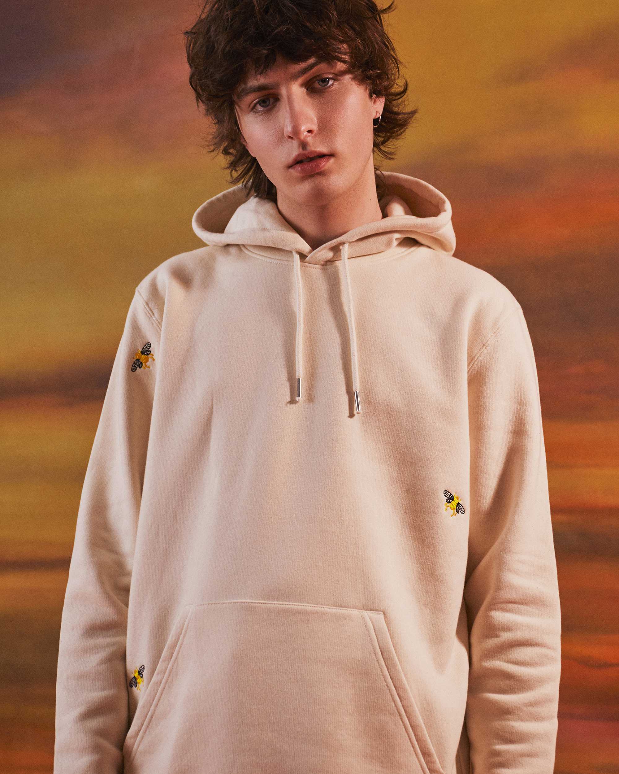A guys wearing a cream hoodie with bees embroidered 