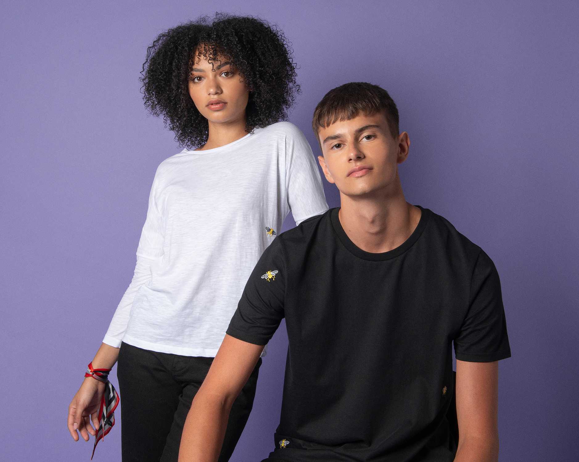 A couple is standing together infront of a purple backdrop wearing monocrome tops with embroideries 