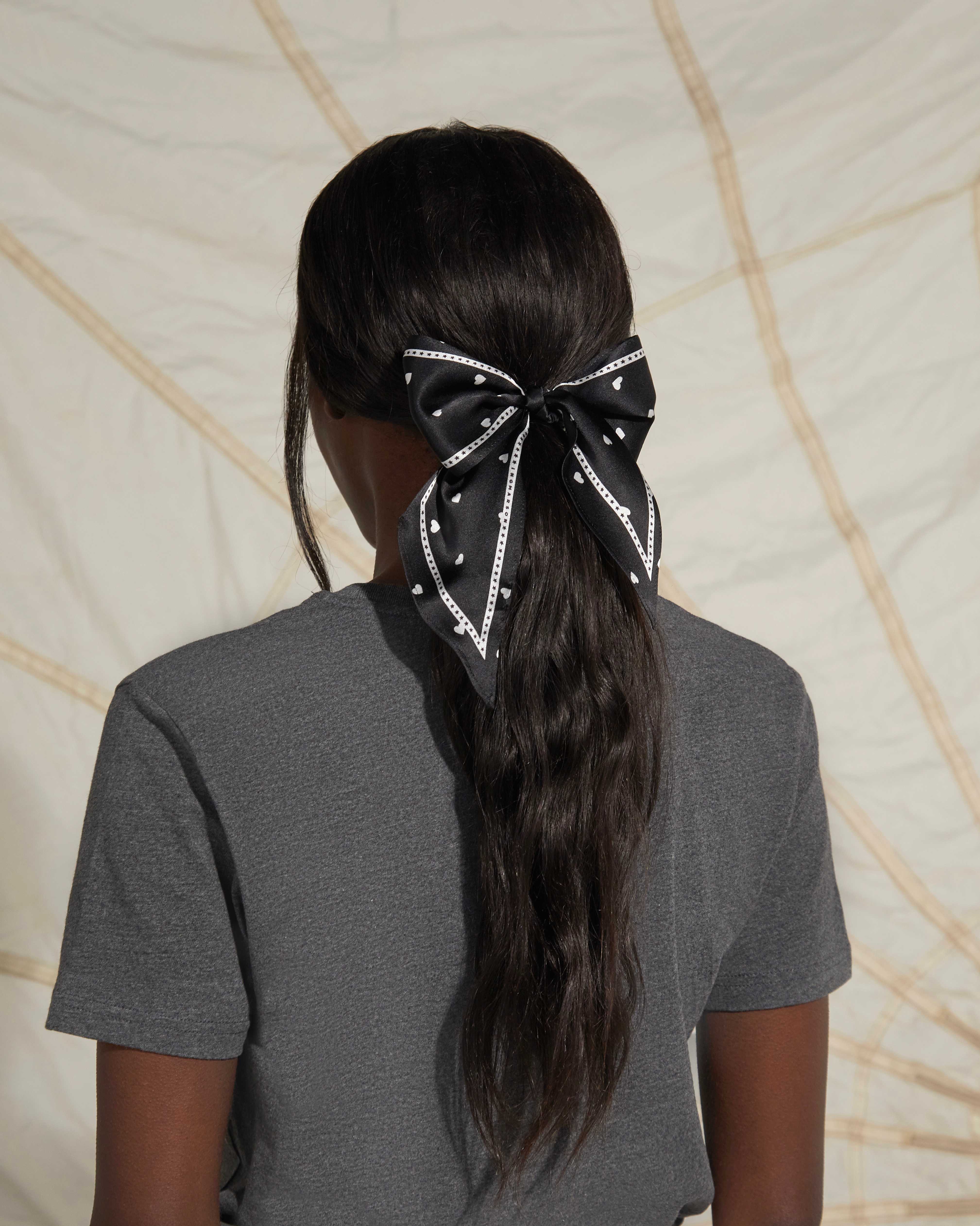 Women wearing a grey top and a black silk scarf in her hair tied as a bow